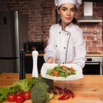 Woman cook with fresh salad in her hands in kitchen