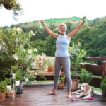 A senior woman standing outdoors on a terrace in summer, doing exercise.