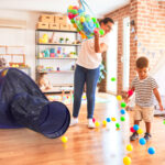 Beautiful teacher and toddler boy playing with colored small balls at kindergarten