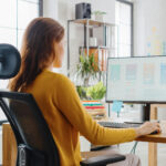 Over the Shoulder: Female Mobile Software Developer Sitting at H