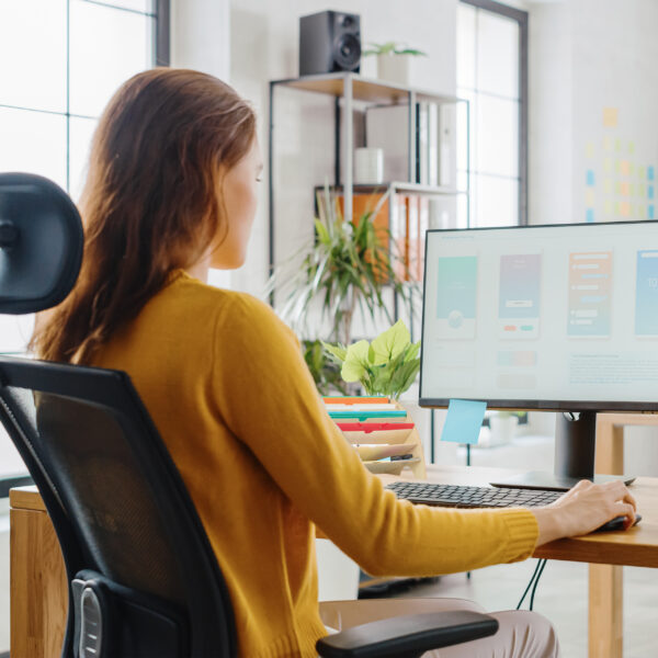 Over the Shoulder: Female Mobile Software Developer Sitting at H