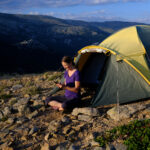 Blode hair woman relaxing outside of a tent using her phone.