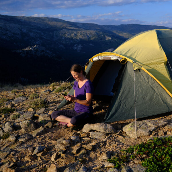 Blode hair woman relaxing outside of a tent using her phone.