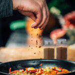 Sprinkling Ground Red Chili Pepper Paprika over Sliced Vegetables