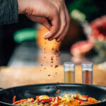 Sprinkling Ground Red Chili Pepper Paprika over Sliced Vegetables