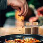 Sprinkling Ground Red Chili Pepper Paprika over Sliced Vegetables
