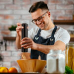 Young man pouring pepper.. Chef preparing salad in modern kitche