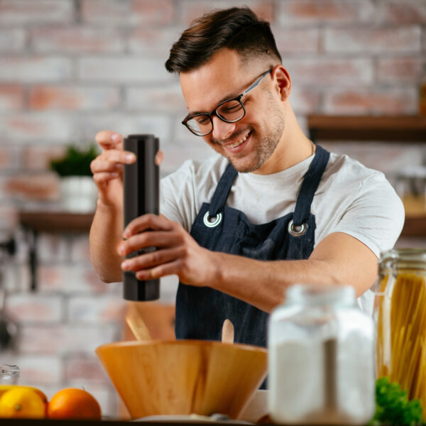 Young man pouring pepper.. Chef preparing salad in modern kitche