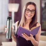 Woman looking at notebook and holding thermo mug