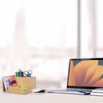Sideview of office desktop with blank laptop and various office tools on wood desk.