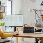 Over the Shoulder: Female Mobile Software Developer Sitting at H