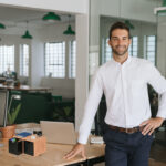 Smiling young businessman leaning against a table in an office