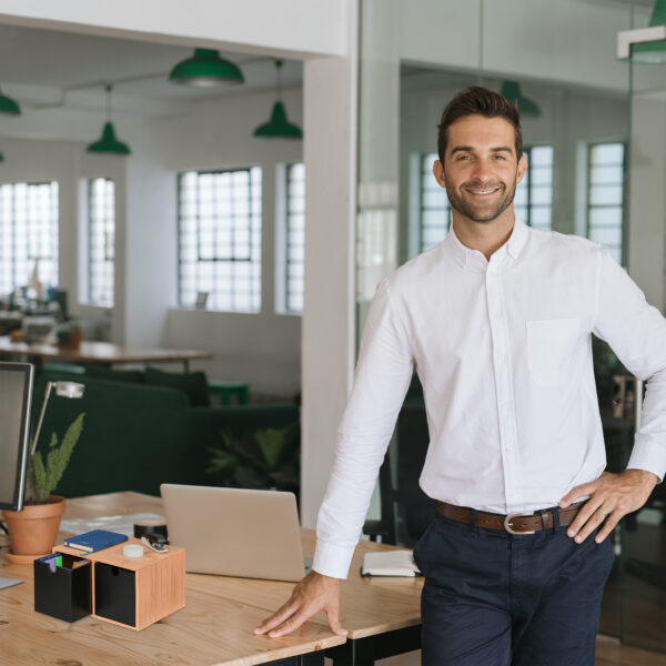 Smiling young businessman leaning against a table in an office